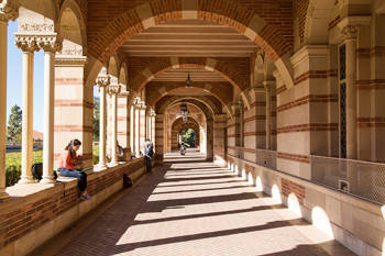 Photo of an outdoor corridor on a university campus which is made of stones and students sit and read on the ledges
